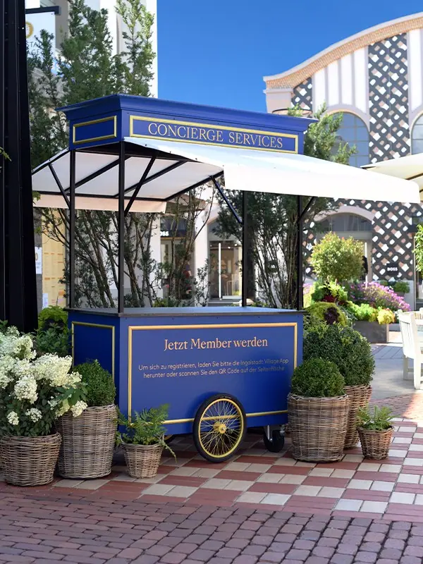 Blauer Concierge-Wagen mit Sonnendach und Blumen auf einem gepflasterten Platz